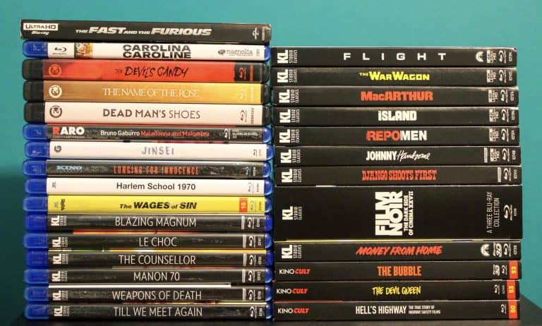 Two stacks of Blu-ray and DVD movie cases are arranged upright against a turquoise background, featuring various film titles on their spines.