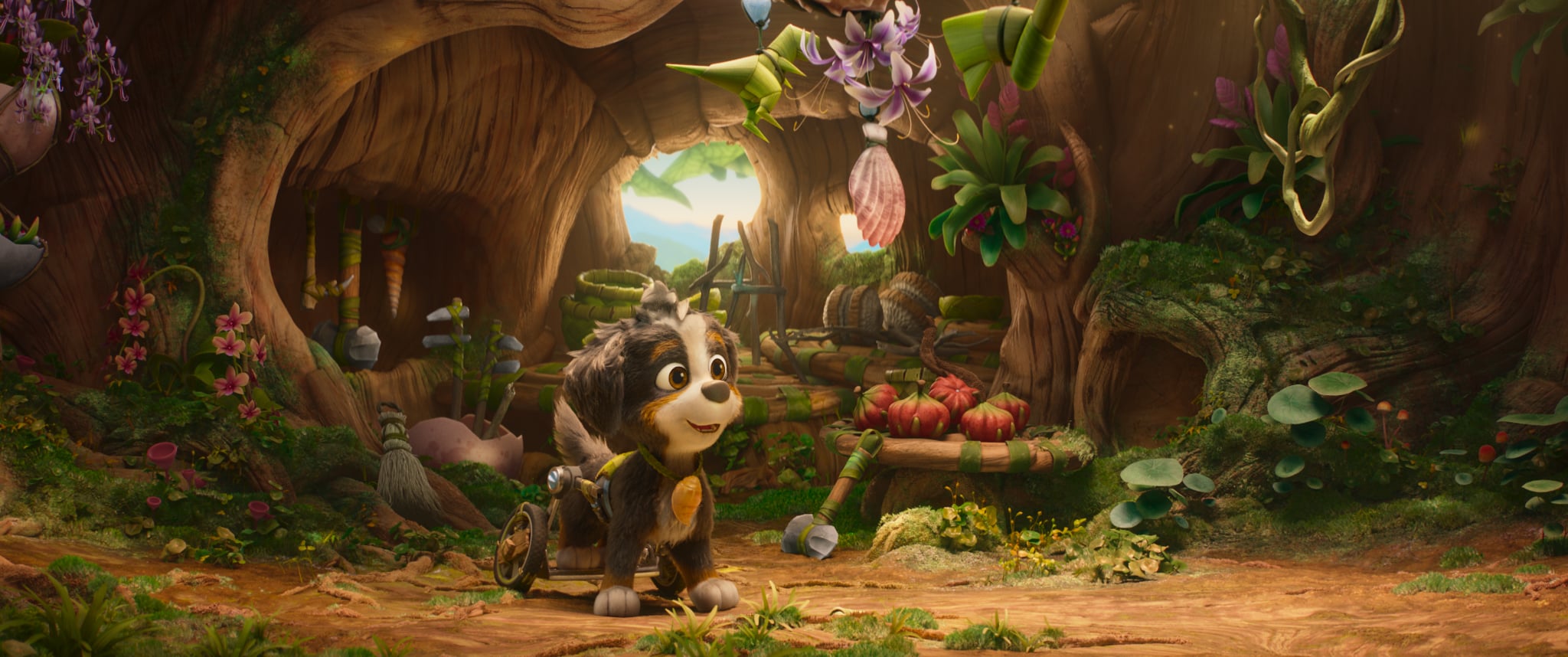 Animated dog with a wheelchair harness sits in a cozy, plant-filled tree hollow with baskets of fruit, leaves, and hanging flowers. Light shines through an opening in the back.