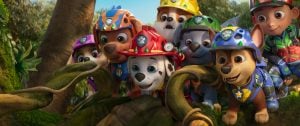‘Paw Patrol: The Dino Movie’ Review – A Dino-Sized Adventure Made For Its Youngest Fans A group of animated puppies in colorful helmets and uniforms gather closely together, looking curiously at something off-screen in a jungle setting.
