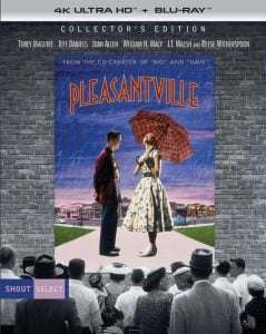 A crowd in black and white watches a colorful movie poster for “Pleasantville” featuring a man and woman under a red umbrella, framed by a brick wall.