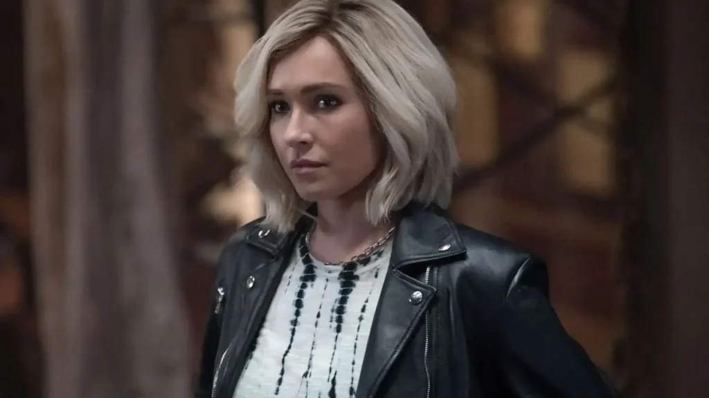Remembering Hayden Panettiere: A Life of Light, Talent, And Quiet Strength Woman with short blonde hair wearing a black leather jacket and white patterned shirt stands indoors, looking to the side with a serious expression.