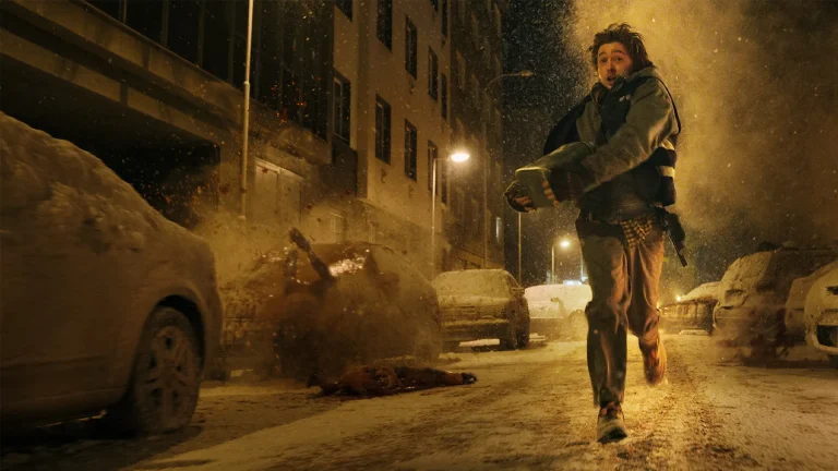 A person runs on a snowy city street at night, carrying a bag, while an explosion occurs behind them, with damaged cars and debris visible.