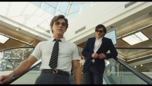 The Shards Two men ride an escalator in a modern mall, one in a white shirt and tie in front, the other in a blue jacket behind, with sunlight streaming through the glass ceiling.