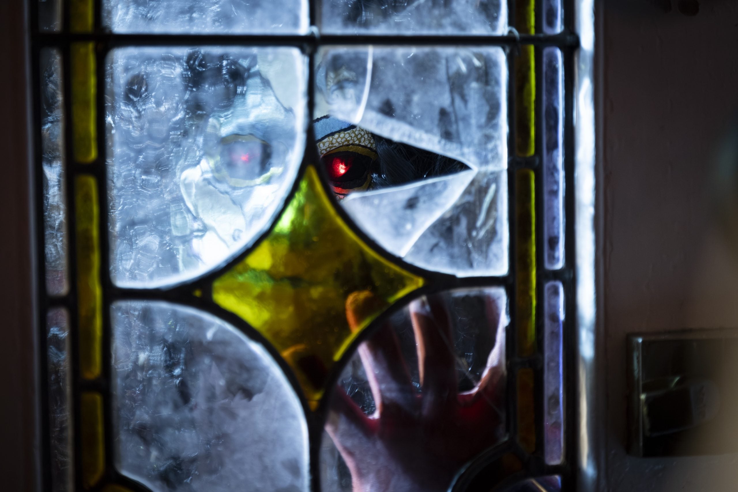 A clawed hand and glowing red eye are visible through a broken stained glass window, suggesting a creature trying to get inside.