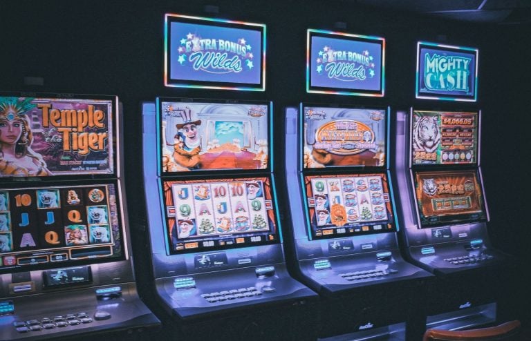 Four brightly lit slot machines in a row, each with colorful screens displaying various game themes and graphics in a casino setting.