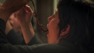 A person pulls a long, dark object from their mouth while looking in a mirror.