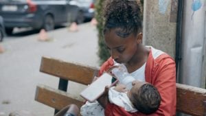‘Young Mothers’ Blu-Ray Review – The Dardenne Brothers Return With Another Effective, Naturalistic Drama A woman sits on a bench, feeding a baby with a bottle while looking at her phone.