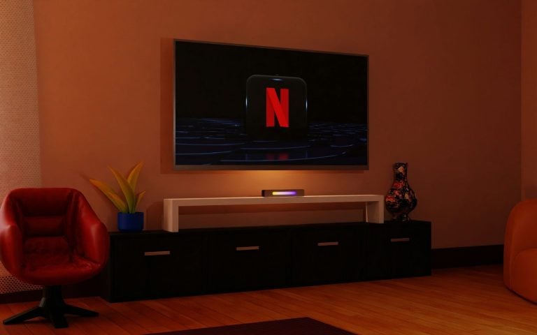 A modern living room with a wall-mounted TV displaying the Netflix logo, a black console with decor items, and red chairs on a wooden floor.