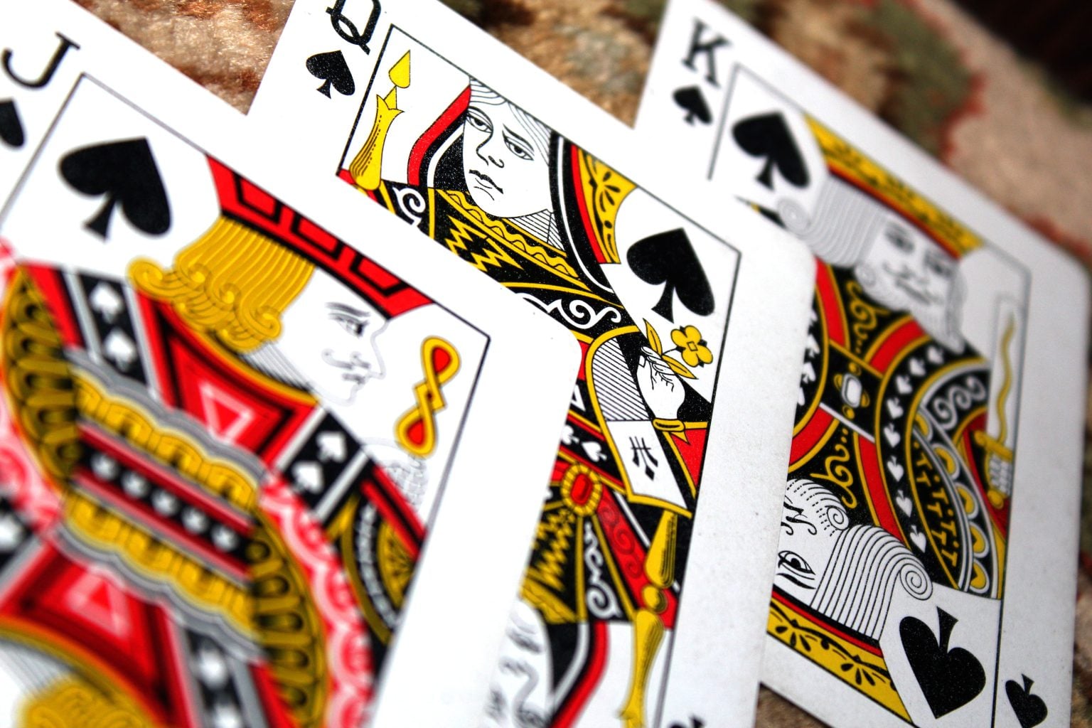 Close-up view of playing cards showing the queen, jack, and king of spades arranged diagonally on a surface.