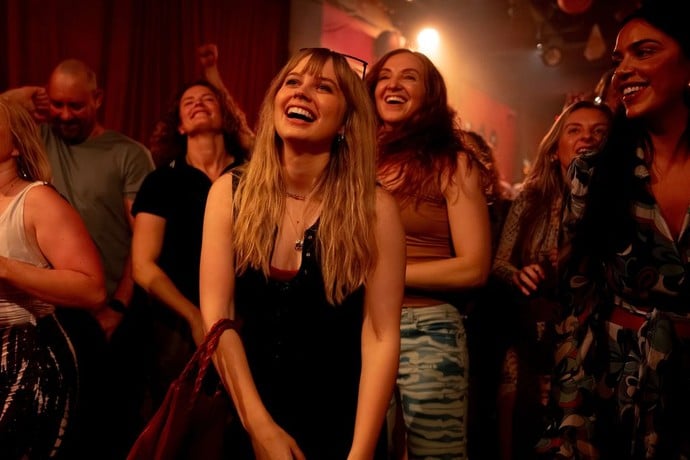 A group of people stand close together at an indoor event, smiling and laughing under warm lighting.