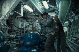 Lionsgate To Release The Jason Statham Action-Thriller ‘Mutiny’ On 4K UHD Blu-Ray This November A man holding a gun leads a woman through a cramped, industrial mechanical room filled with pipes, machinery, and overhead lights.