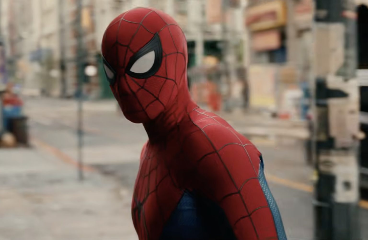 A person in a red and blue Spider-Man costume stands on a city street, looking toward the camera.