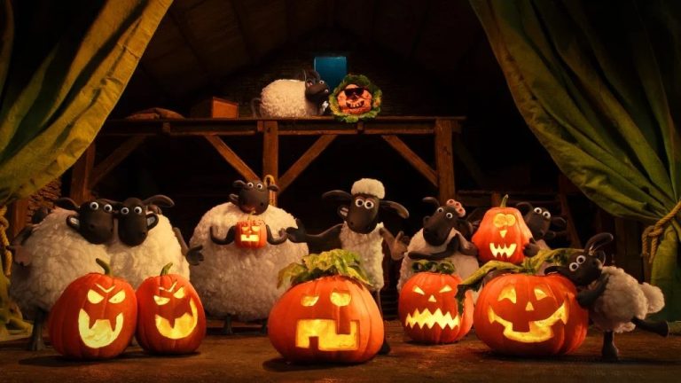 ‘Shaun The Sheep: The Beast Of Mossy Bottom’ Review – A Perfect Dose Of Spooky Stop-Motion Charm Animated sheep stand in a barn surrounded by carved, glowing jack-o’-lanterns with various facial expressions, indicating a Halloween celebration.