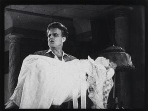 Czech Silent Genre Rarities From Director Jan S. Kolár Blu-Ray Review – A Genre-Bending Duo From The Silent Era A man in period clothing holds an unconscious or lifeless woman in his arms inside an ornate room with columns and a lamp.