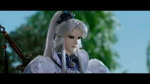 A white-haired puppet with elaborate clothing and a sword on its back stands outdoors with trees blurred in the background.