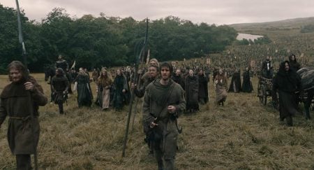 Universal To Release The Andrew Garfield Historical Action Drama ‘The Uprising’ On 4K UHD Blu-Ray This November A large group of people in medieval clothing walks through a grassy field, holding spears and banners, with trees and hills in the background.