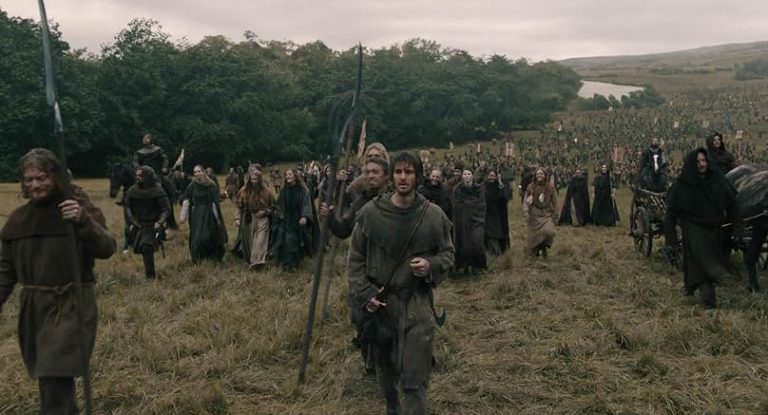 Universal To Release The Andrew Garfield Historical Action Drama ‘The Uprising’ On 4K UHD Blu-Ray This November A large group of people in medieval clothing walks through a grassy field, holding spears and banners, with trees and hills in the background.