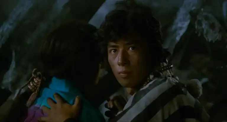 ‘Ninja Wars’ Blu-Ray Review – Hiroyuki Sanada Wades Into The Supernatural In This Brutal Action Outing A man in a striped garment looks forward while holding another person close; the background is dark and out of focus.