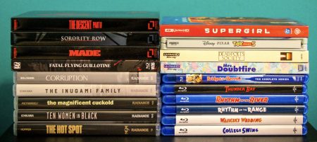 No Streaming Required: Physical Media Spotlight For The Week Of September 22nd Stacks of DVD and Blu-ray movie cases arranged side by side on a flat surface against a teal background.