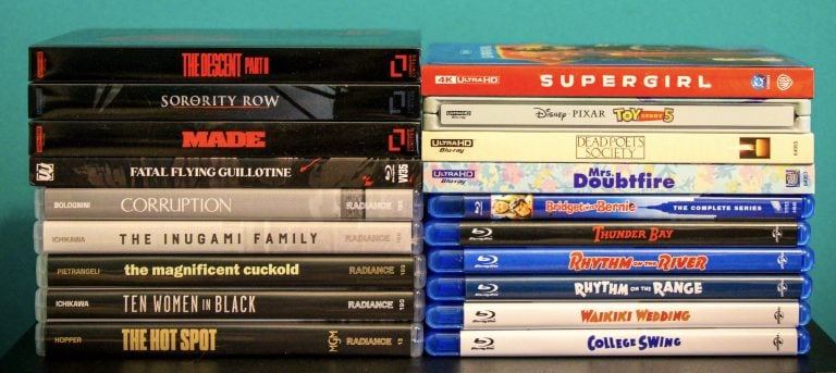 No Streaming Required: Physical Media Spotlight For The Week Of September 22nd Stacks of DVD and Blu-ray movie cases arranged side by side on a flat surface against a teal background.