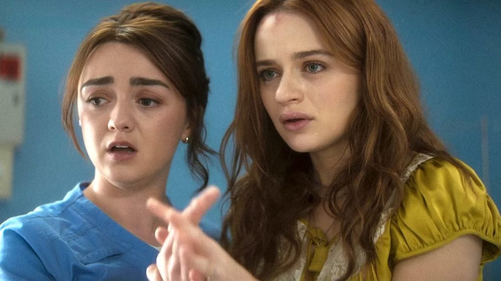 Two young women stand close together indoors, looking intently in the same direction; one wears blue scrubs, the other a yellow top, both with concerned facial expressions.