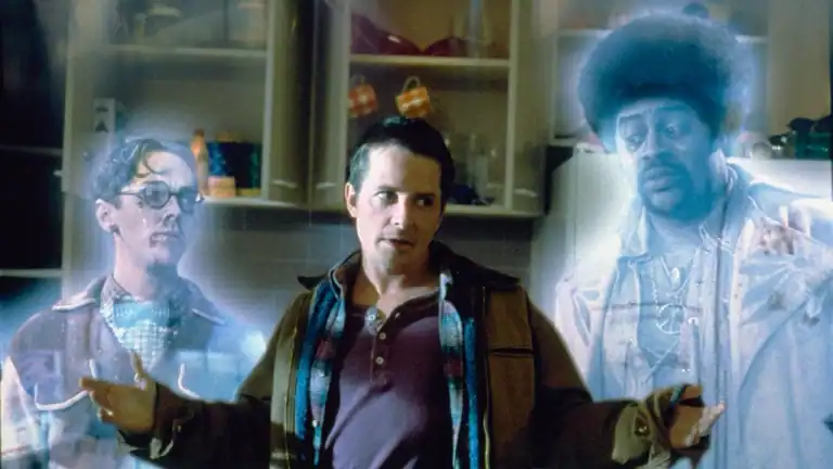 A man stands in a kitchen with his arms outstretched, flanked by two ghostly figures glowing with a blue tint.
