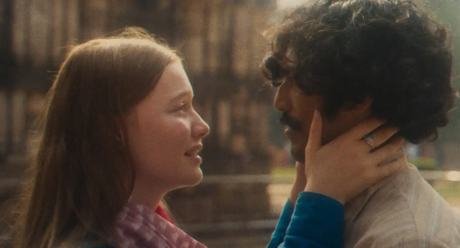A woman gently holds a man’s face with both hands while looking at him closely outdoors.