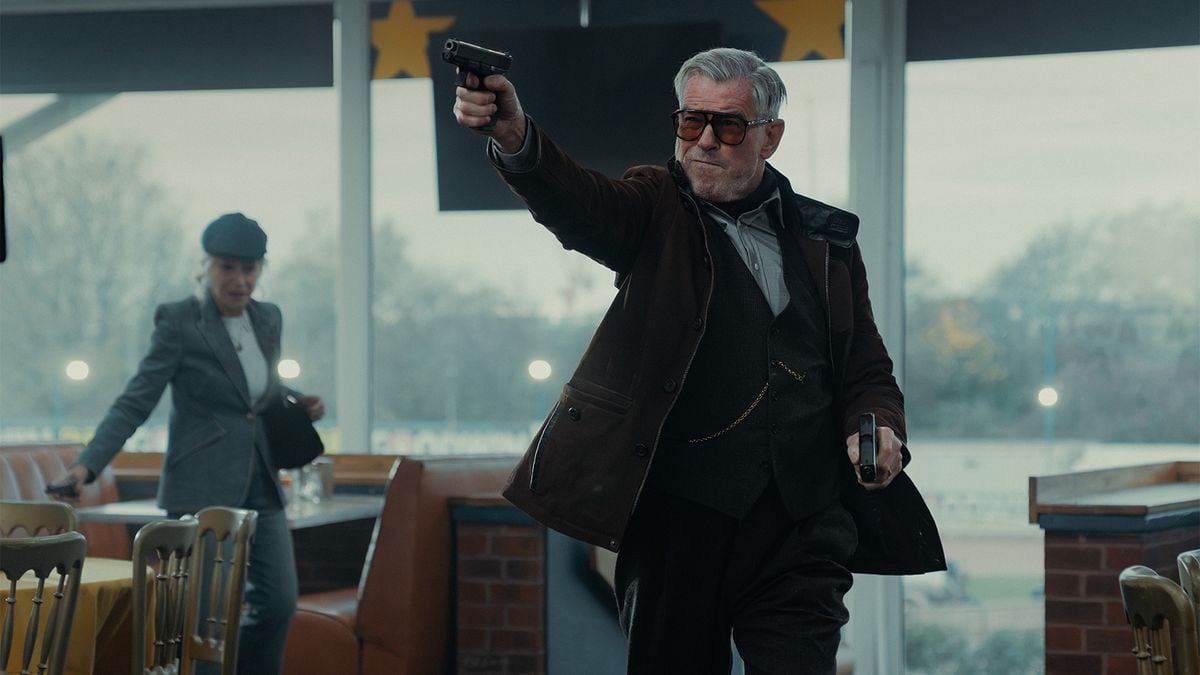 Older man in a suit and glasses points a handgun inside a diner, while a woman in a hat stands behind him near booths and tables.