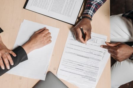 How A Reliable Online PDF Editor Fixes A Broken Document Management Workflow Two people sit at a desk with documents; one is signing a form while the other points at the paperwork.