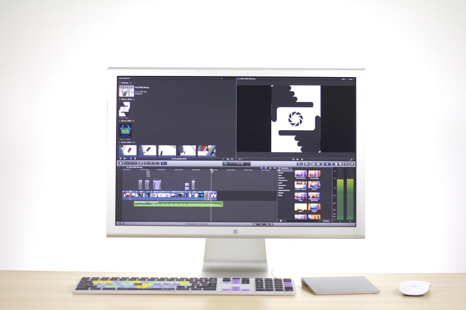 A computer monitor displaying video editing software sits on a desk with a keyboard, mouse, and trackpad in front of it.