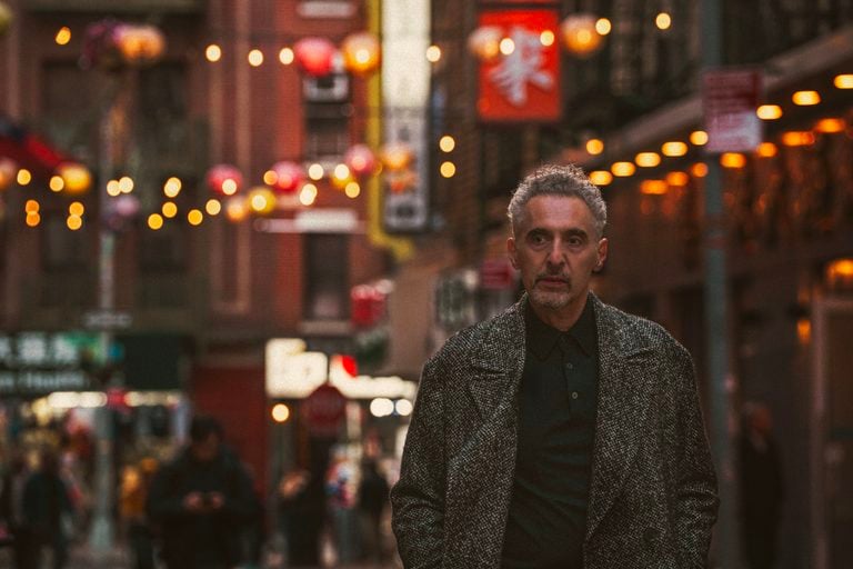 A man in a textured coat walks down a city street decorated with hanging lanterns.