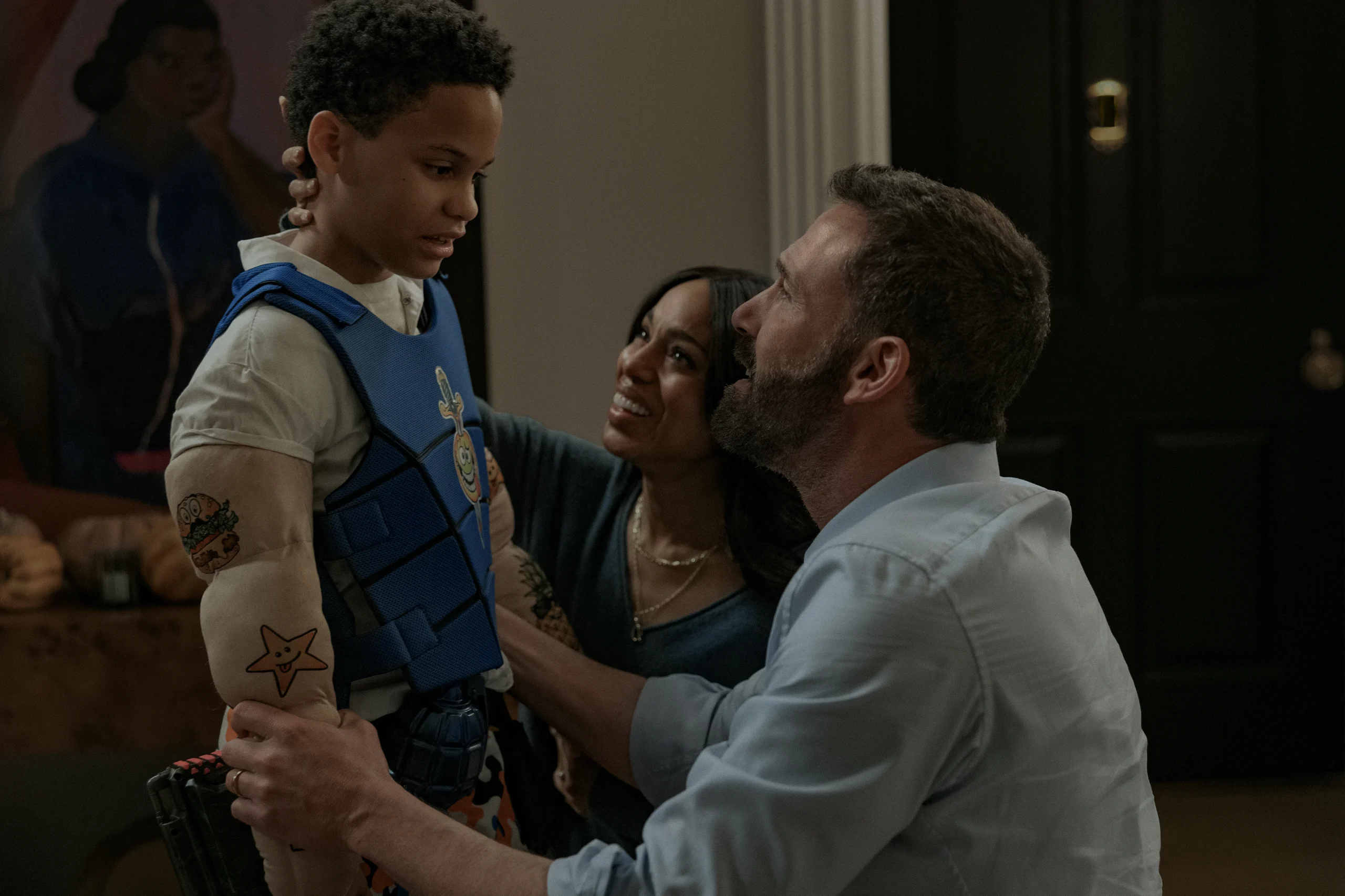 A man and a woman look at a young boy wearing a blue tactical vest and a toy arm sleeve with cartoon graphics.