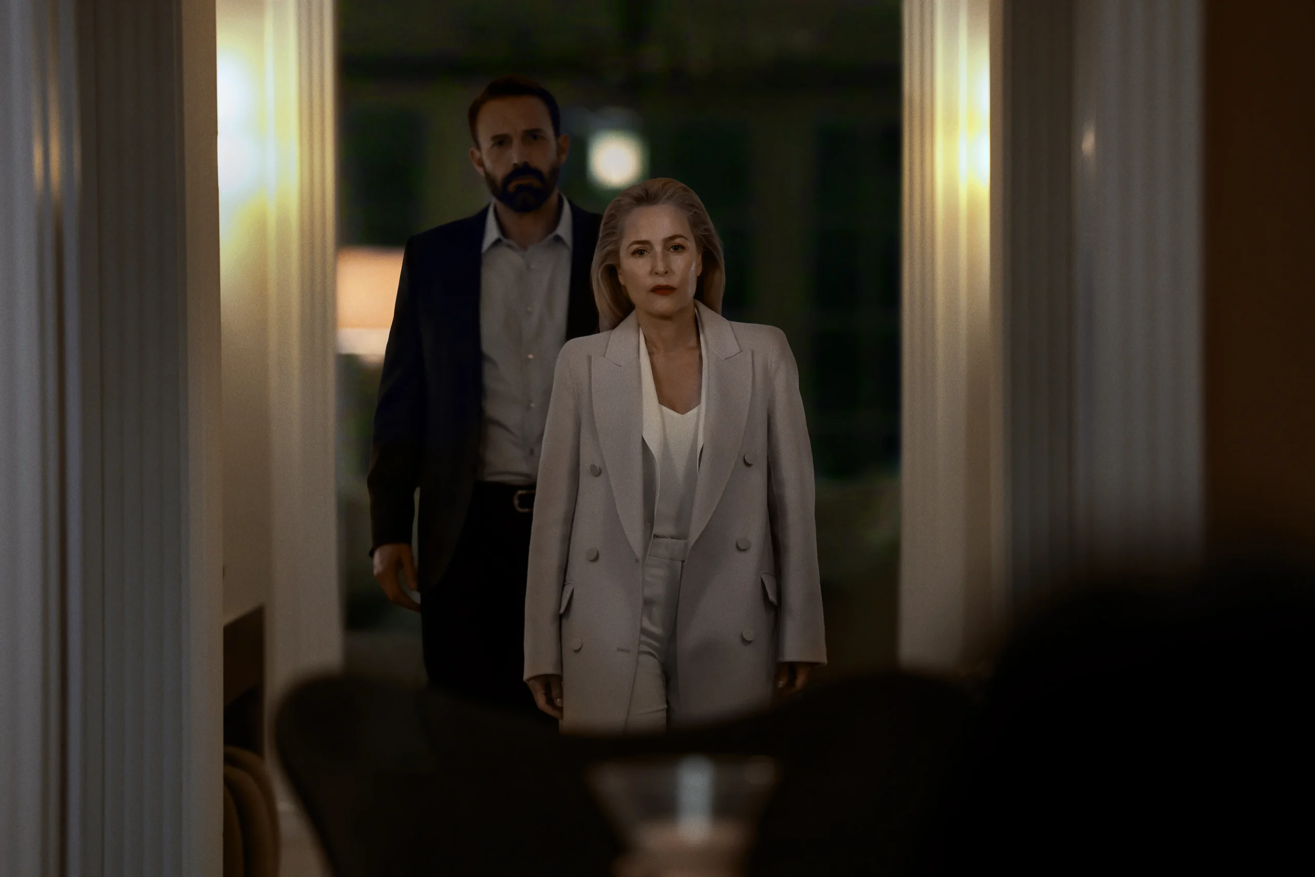 A woman in a light-colored suit and a man in a dark suit standing in a doorway.