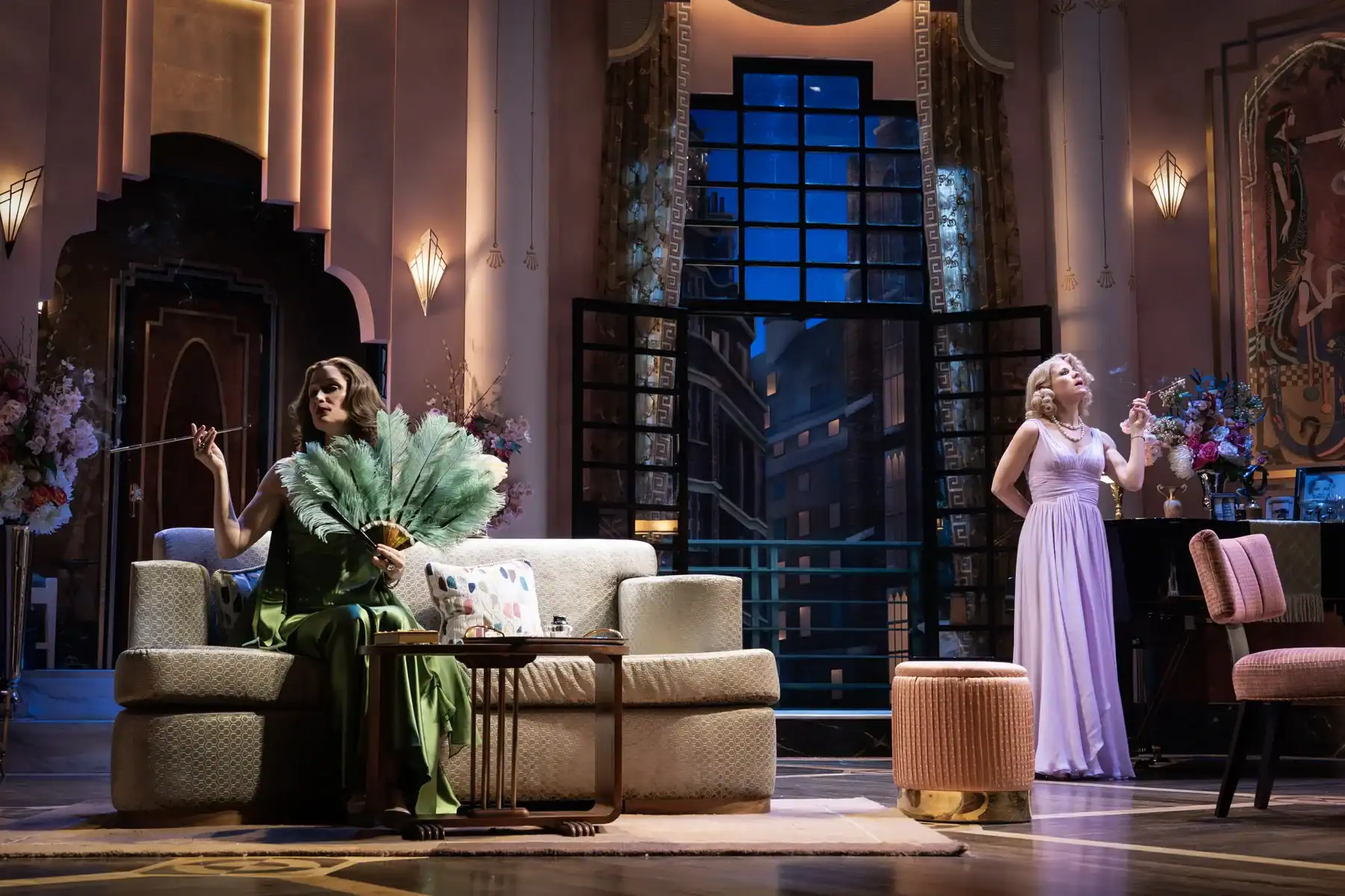 Two women in evening gowns pose in an Art Deco-style room, each holding a cigarette holder.
