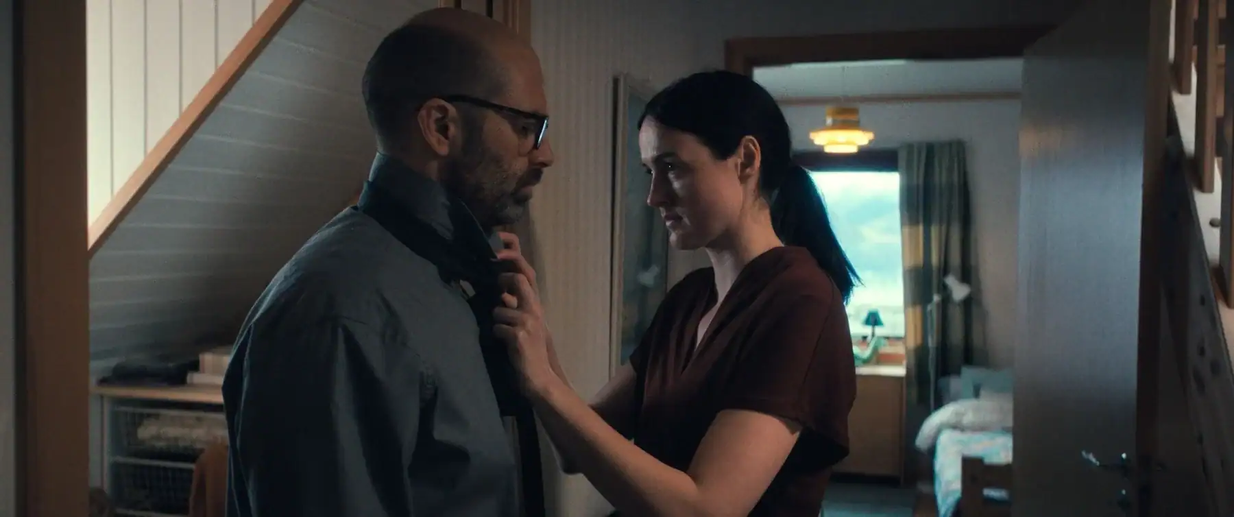 A woman adjusts a man’s necktie while standing in a hallway.