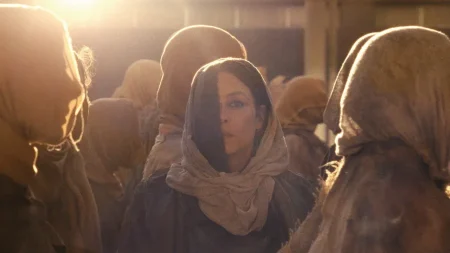 A woman wearing a headscarf surrounded by other people in headscarves, backlit by a bright light source.