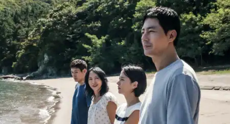 Four people stand in a line on a beach, looking toward the horizon.