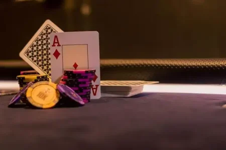 An ace of diamonds playing card leaning against a stack of purple poker chips next to a pile of yellow chips on a dark table.