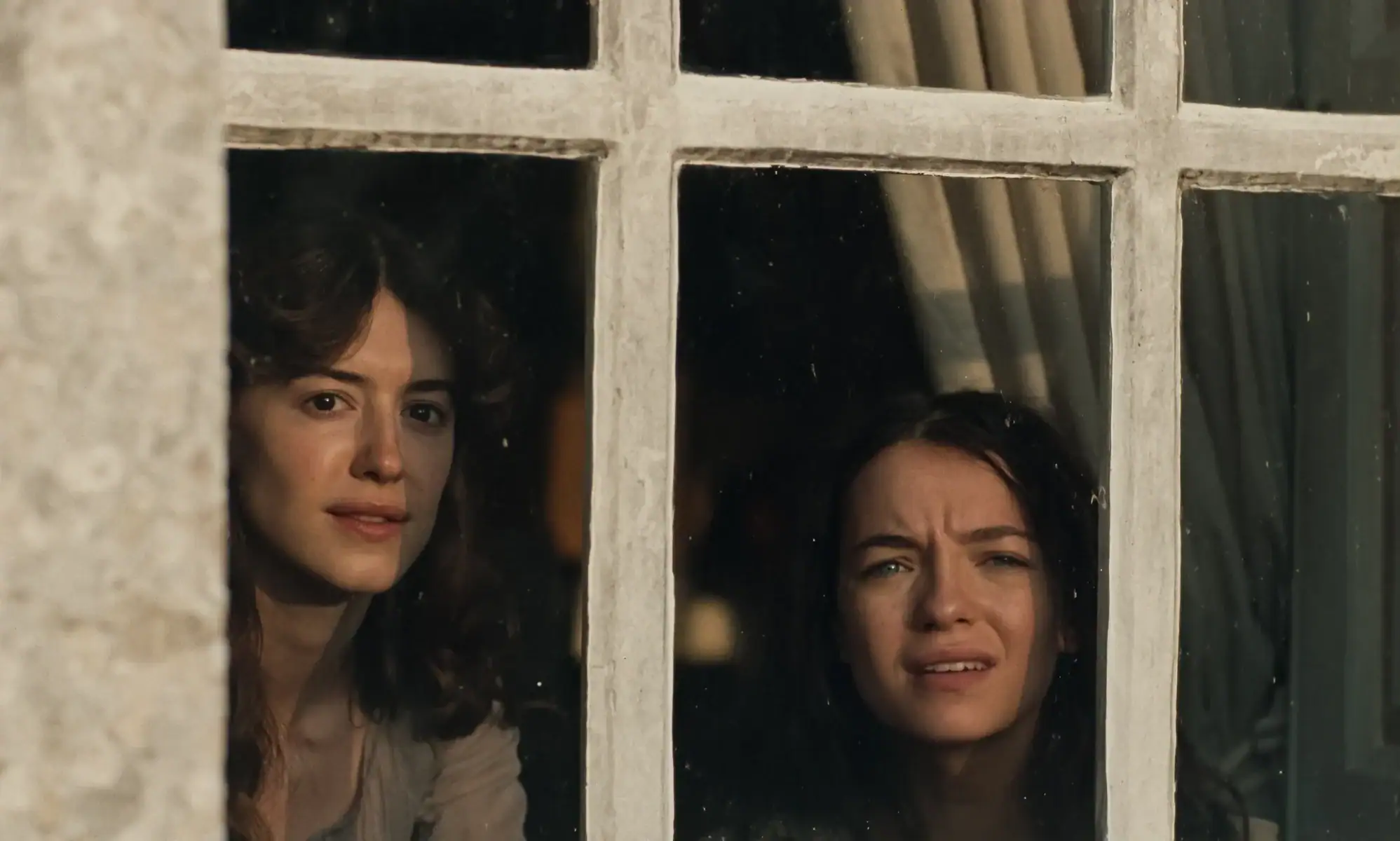 Two women looking out through a window pane.