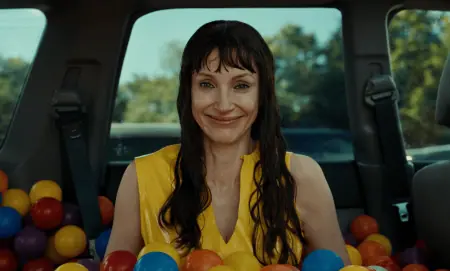 A woman in a yellow top smiles while sitting in the trunk of a car filled with colorful plastic balls.