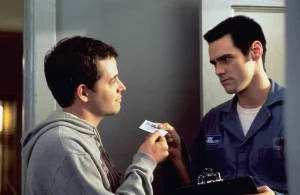 ‘The Cable Guy’ 4K UHD Blu-Ray SteelBook Review – Jim Carrey’s Dark Side Delivers A Barrage Of Uncomfortable Laughs A man in a grey hoodie looks at a business card being held by a man in a blue uniform.