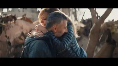 A man and a woman embracing each other amidst the ruins of a destroyed building.