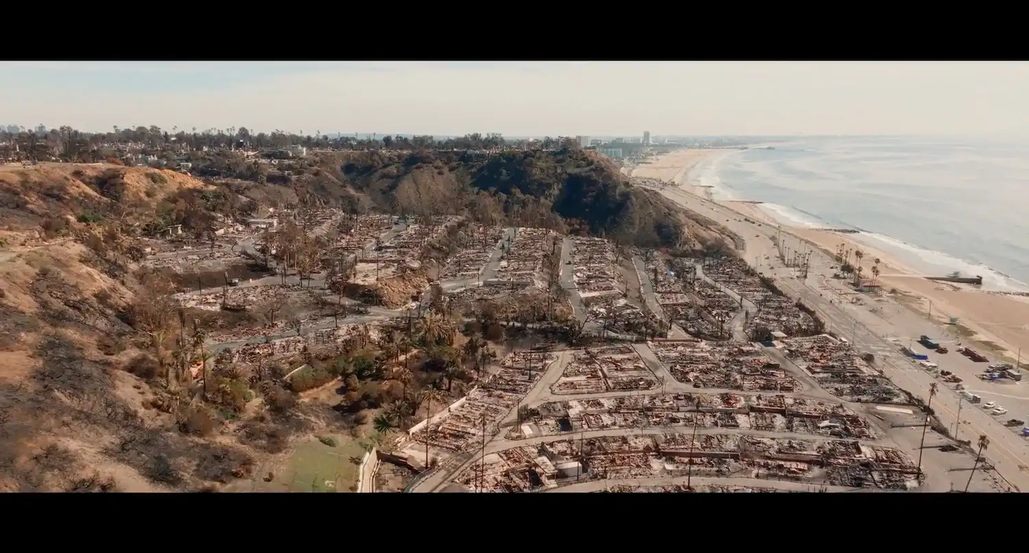 Aerial view of a coastal neighborhood destroyed by fire, adjacent to a beach and highway.