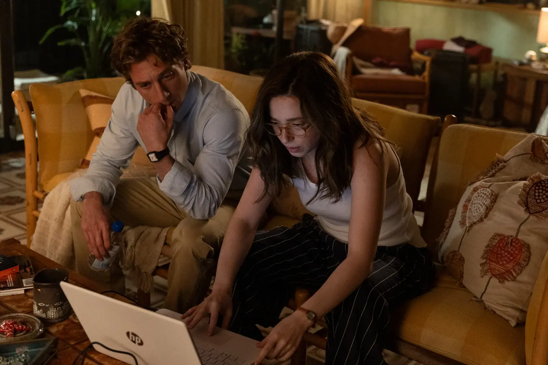 A man and a woman sitting on a couch together, looking at a laptop computer.