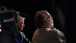 ‘MegaDoc’ Blu-Ray Review – A Compelling Tale Of Boundless Creative Ambition Francis Ford Coppola, in a sweater and glasses, looking off-camera next to a camera operator.