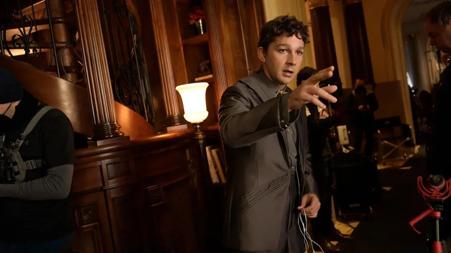 Shia LaBeouf in a suit gesturing while on a film set.