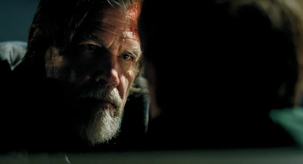A bearded man with a bloodied forehead looks intensely toward an unseen person in the foreground.