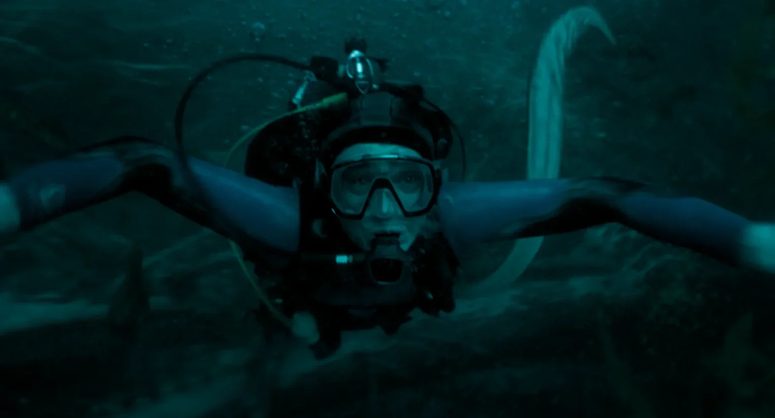 A scuba diver swimming through dark, murky water.