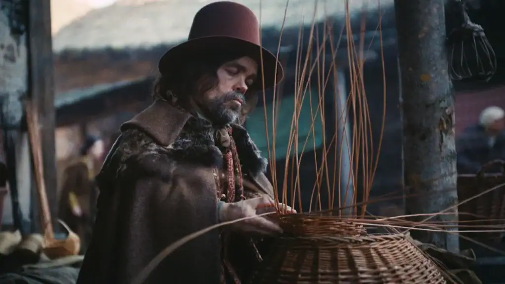 A person wearing a wide-brimmed hat and a cloak weaves a willow basket.