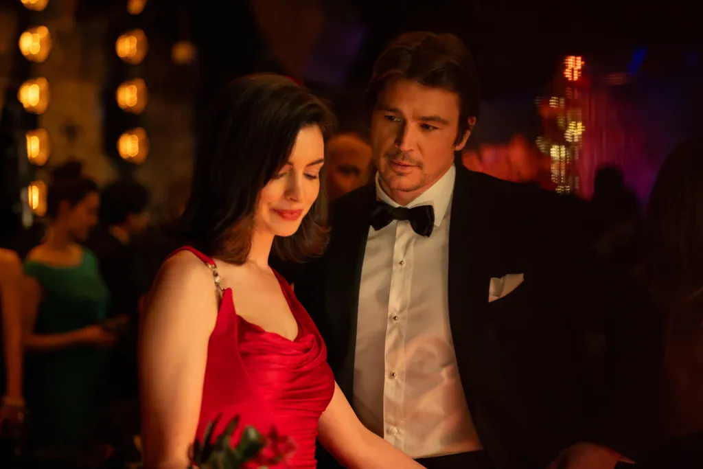 A woman in a red dress and a man in a tuxedo standing together in a dimly lit room.